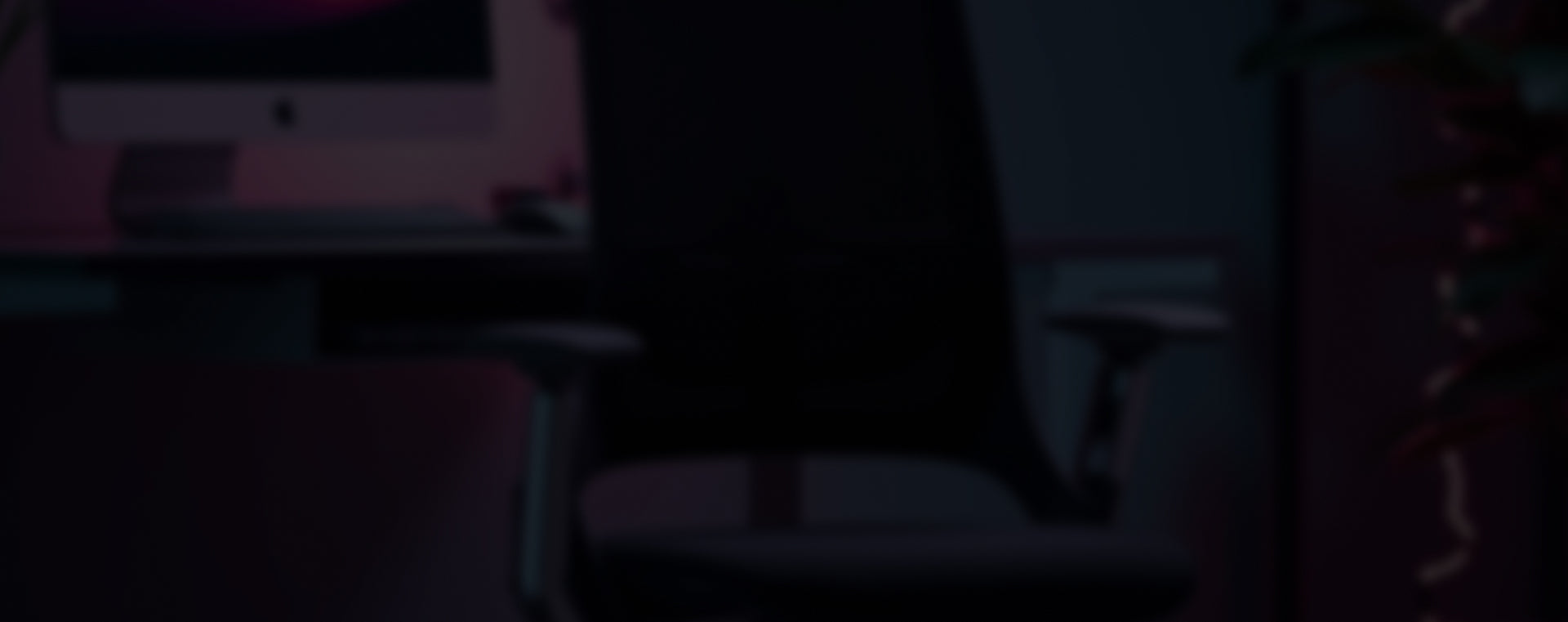 Dunkles Büro mit schwarzem Bürostuhl, silbernem iMac und Tastatur, beleuchtet von pinkem Licht.