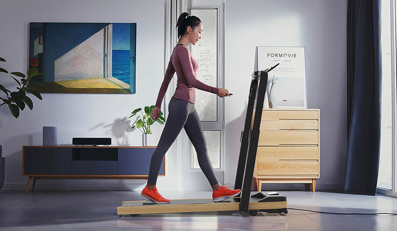 Junge Frau in Sportkleidung geht auf einem schlanken, faltbaren Laufband in einem modernen Wohnzimmer.