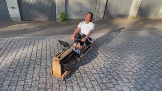 Video: Frau rudert im Freien auf dem TWHEELS Wasserrudergerät aus Eichenholz, mit Rudersitz und Wassertank im Bild.
